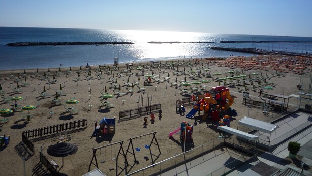 Una playa con numerosos sombrillas y tumbonas, un parque infantil y vistas al mar.