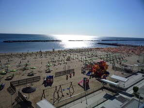A beach with numerous umbrellas and sun loungers, a playground, and a view of the sea. - Albergo Aquila (Rimini)