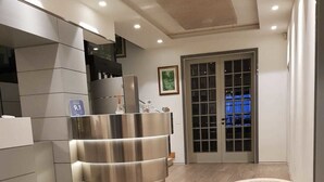 Un interior moderno con una recepción, un área de estar con una mesa de vidrio y una puerta que da al exterior.
