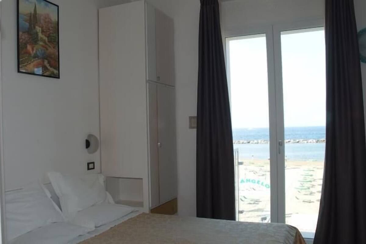 A bedroom with a bed, a wardrobe, and a view of the beach.