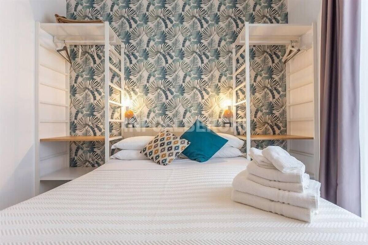 A neatly made bed with white linens and a blue pillow, flanked by white shelves with folded towels.