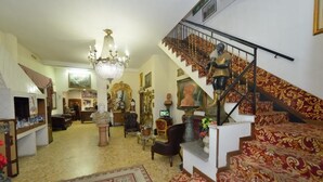 A spacious living room with a grand chandelier, a staircase with ornate carpet, and a variety of furniture including a sofa and armchairs.