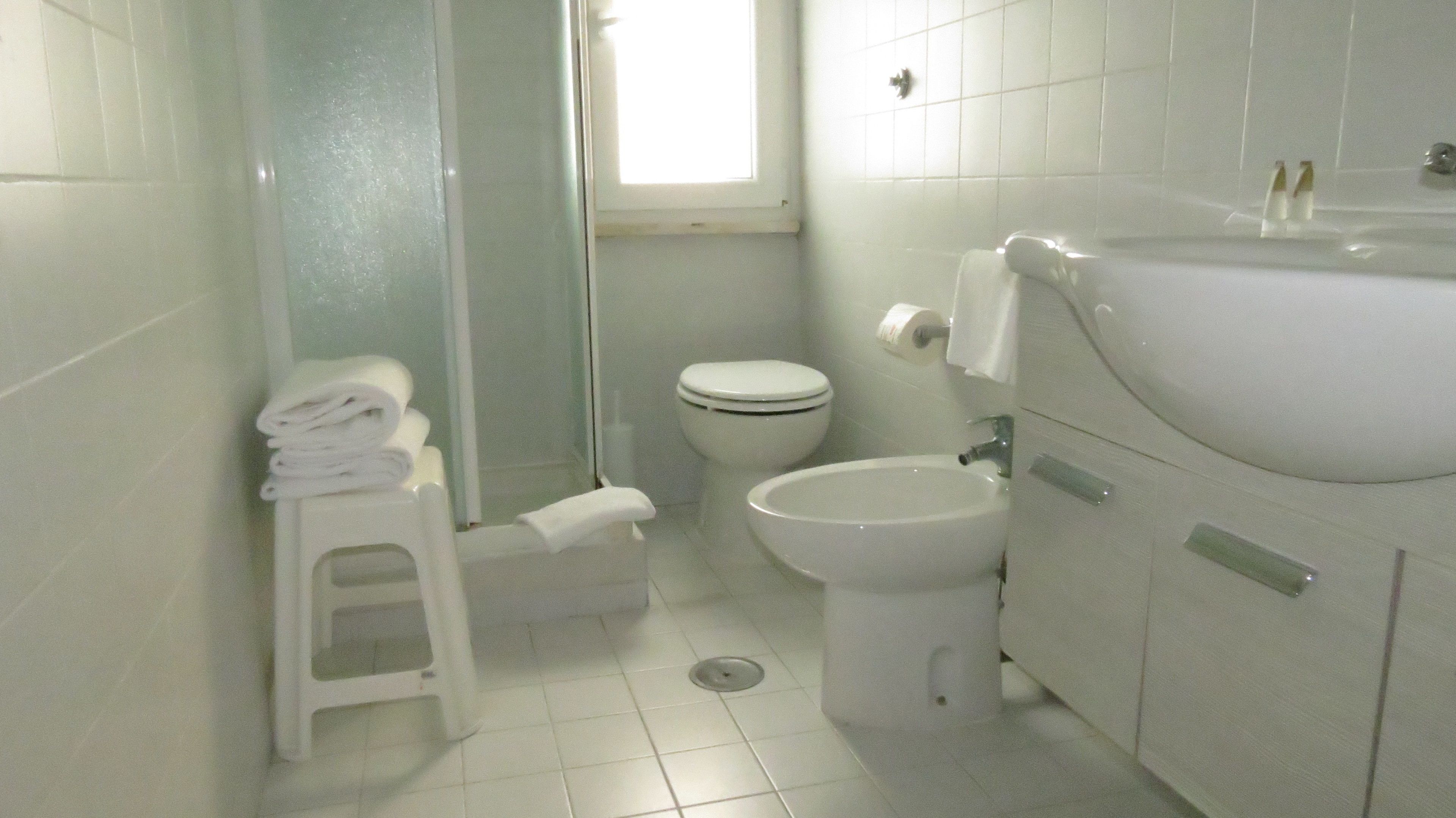 A bathroom with a toilet, sink, and a small stool with towels.