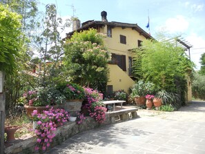 A yellow building with a stone bench in front, surrounded by potted plants and flowers. - Agriturismo Le Macine (Florence)