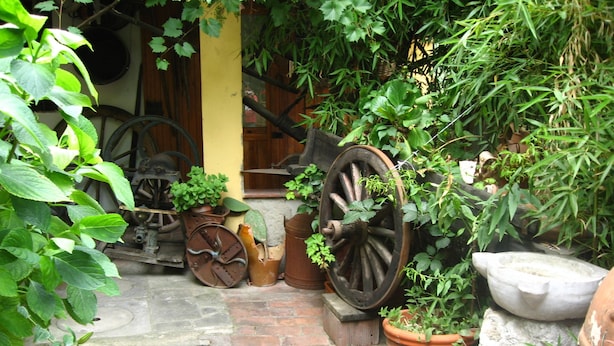 A courtyard with a brick pathway, potted plants, and old-fashioned wheels.