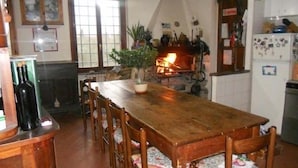 A rustic kitchen with a wooden table, chairs, a fireplace, and a refrigerator.