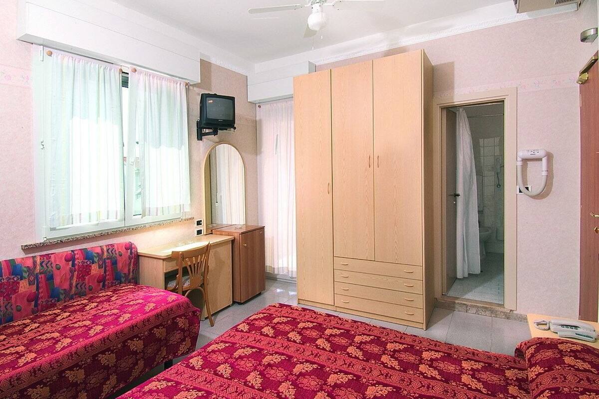 A bedroom with two beds, a desk, a wardrobe, a television, and a bathroom.