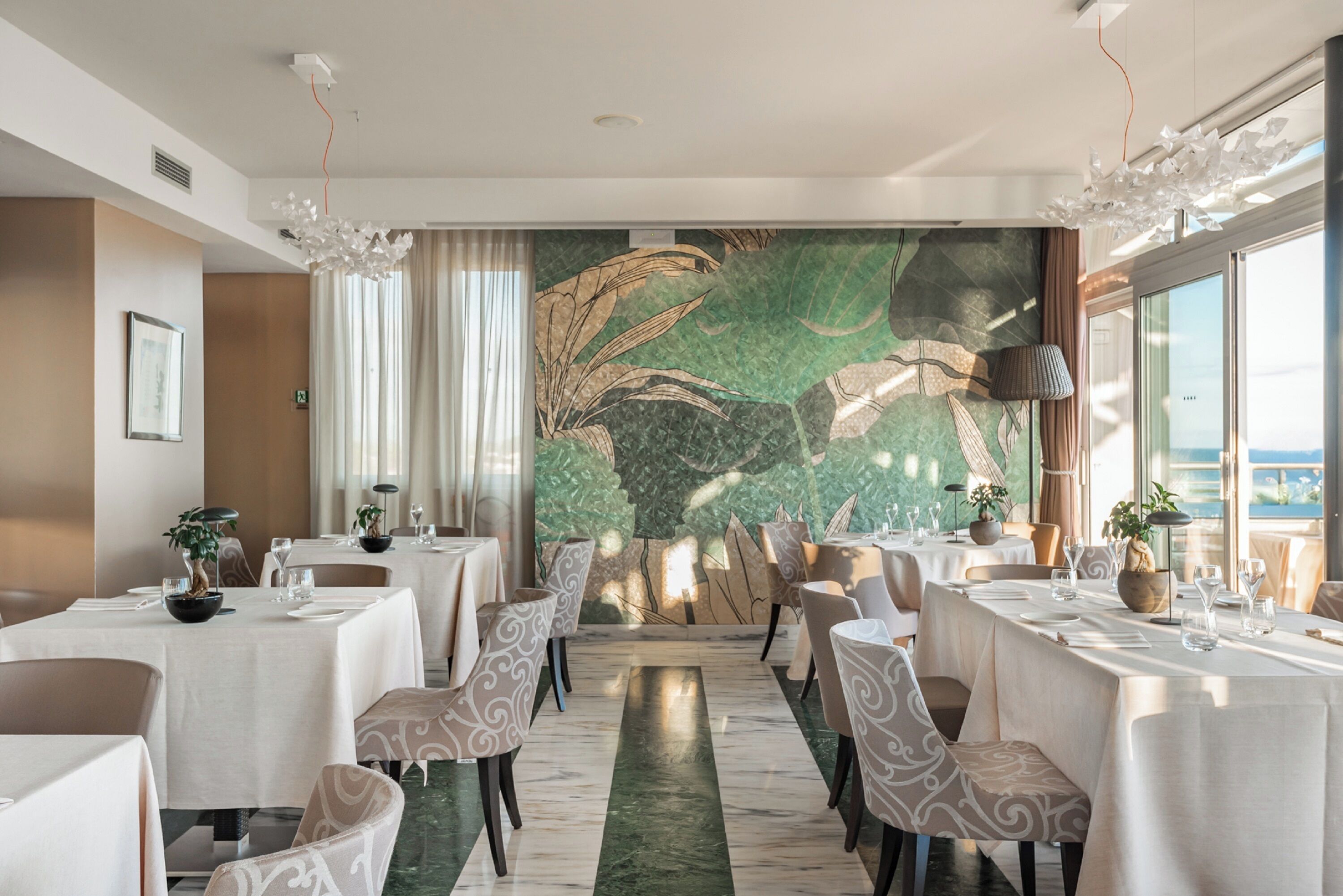 Un comedor con mesas dispuestas para el servicio, un gran muro decorativo y vistas a través de una ventana.