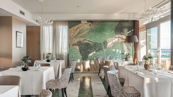 Un comedor con mesas dispuestas para el servicio, un gran muro decorativo y vistas a través de una ventana.