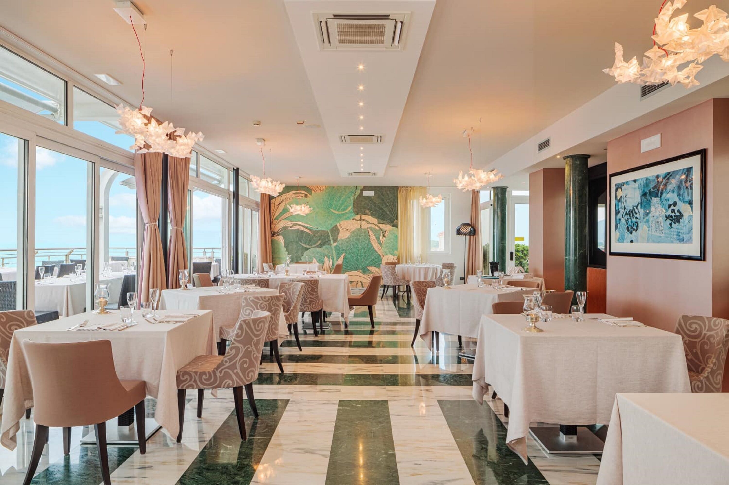 A restaurant with tables set for dining, a mural on the wall, and large windows offering a view.