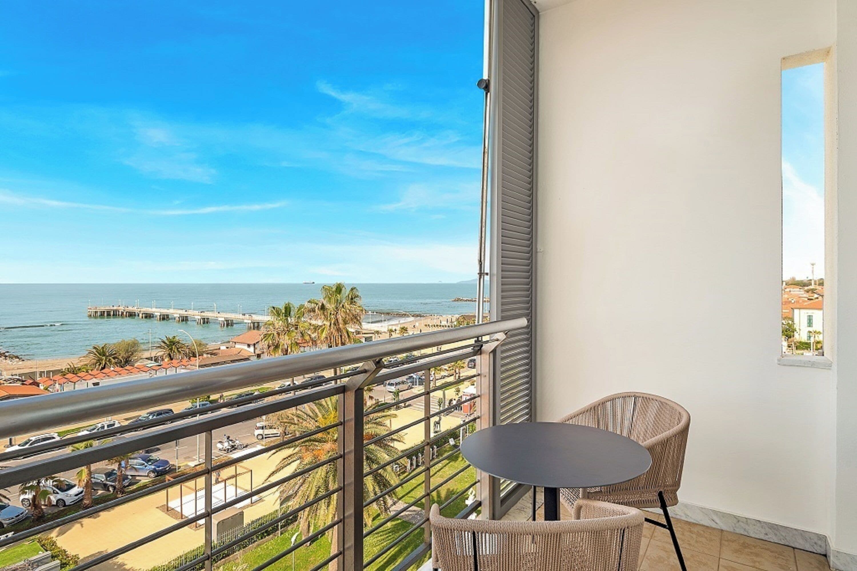 Een balkon met uitzicht op het strand en de pier, een ronde tafel en rieten stoelen.