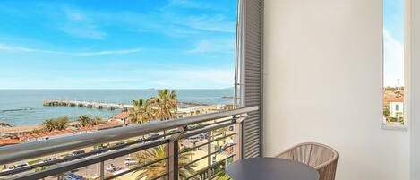 Een balkon met uitzicht op het strand en de pier, een ronde tafel en rieten stoelen.