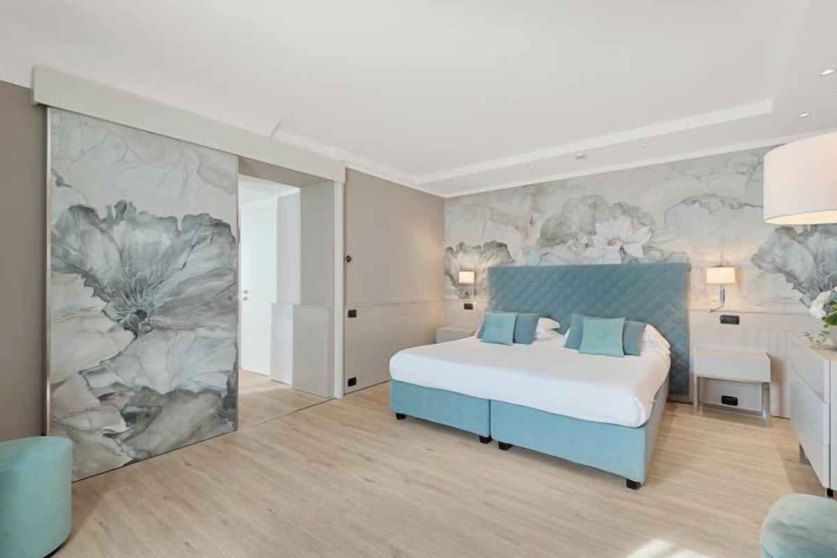 A modern bedroom with a bed, bedside tables, and a large abstract painting on the wall.