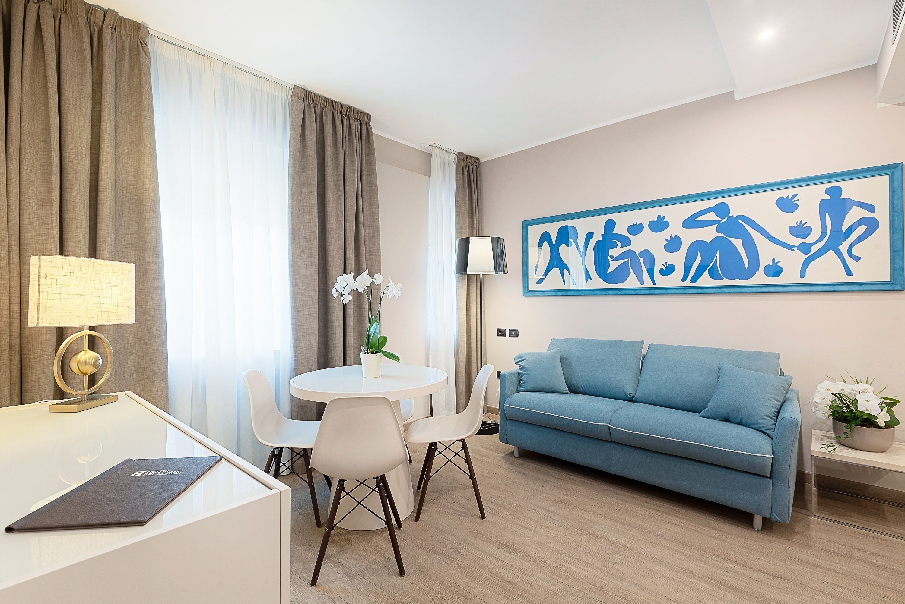 Un soggiorno moderno con un divano blu, un tavolo da pranzo rotondo con sedie, una lampada e un'opera d'arte a parete.