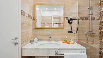 Un baño con lavamanos de mármol, un espejo, toallero, ducha con cabezal de ducha manual y un inodoro.