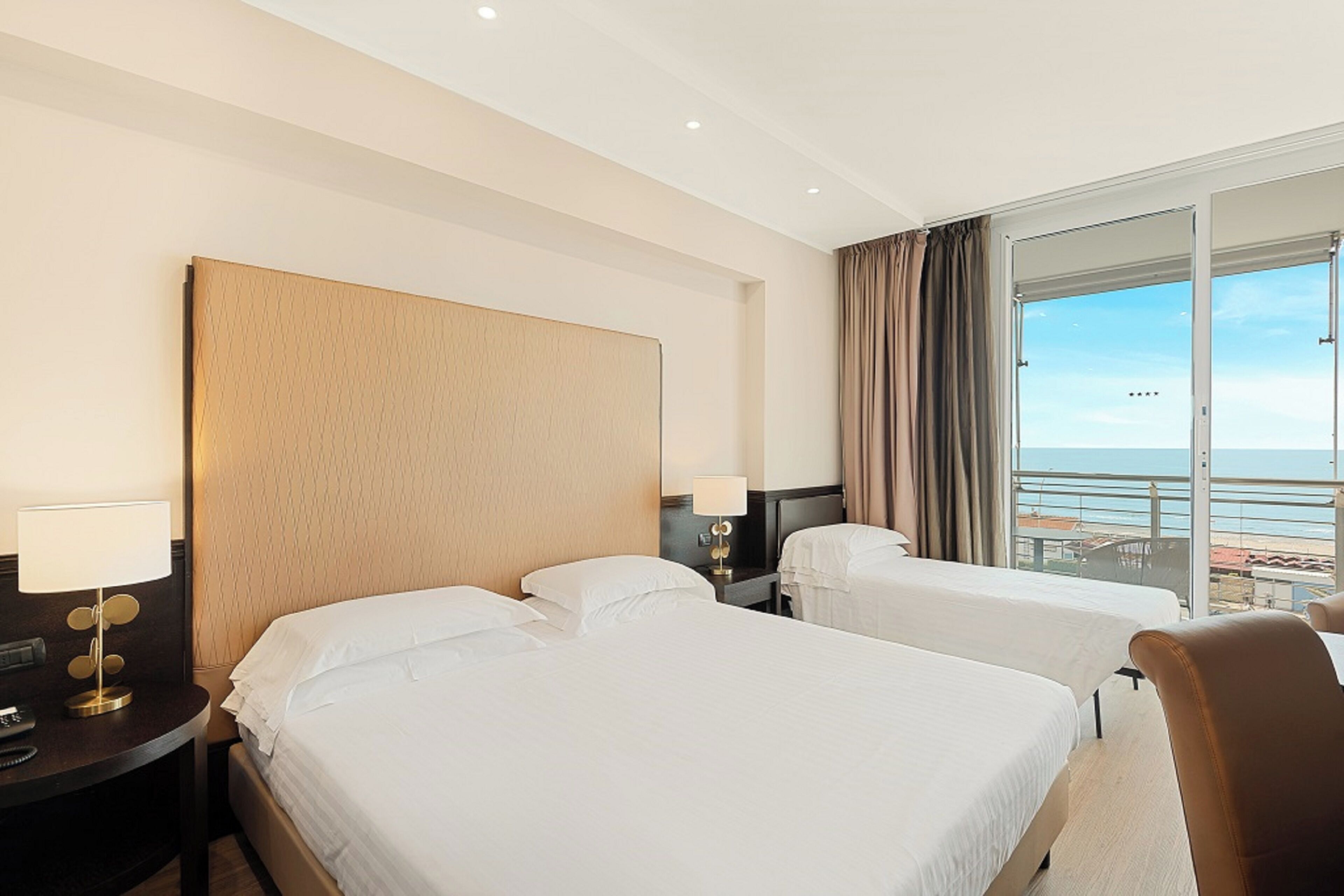 Une chambre d’hôtel avec deux lits, un bureau, une chaise et une grande fenêtre donnant sur la mer.