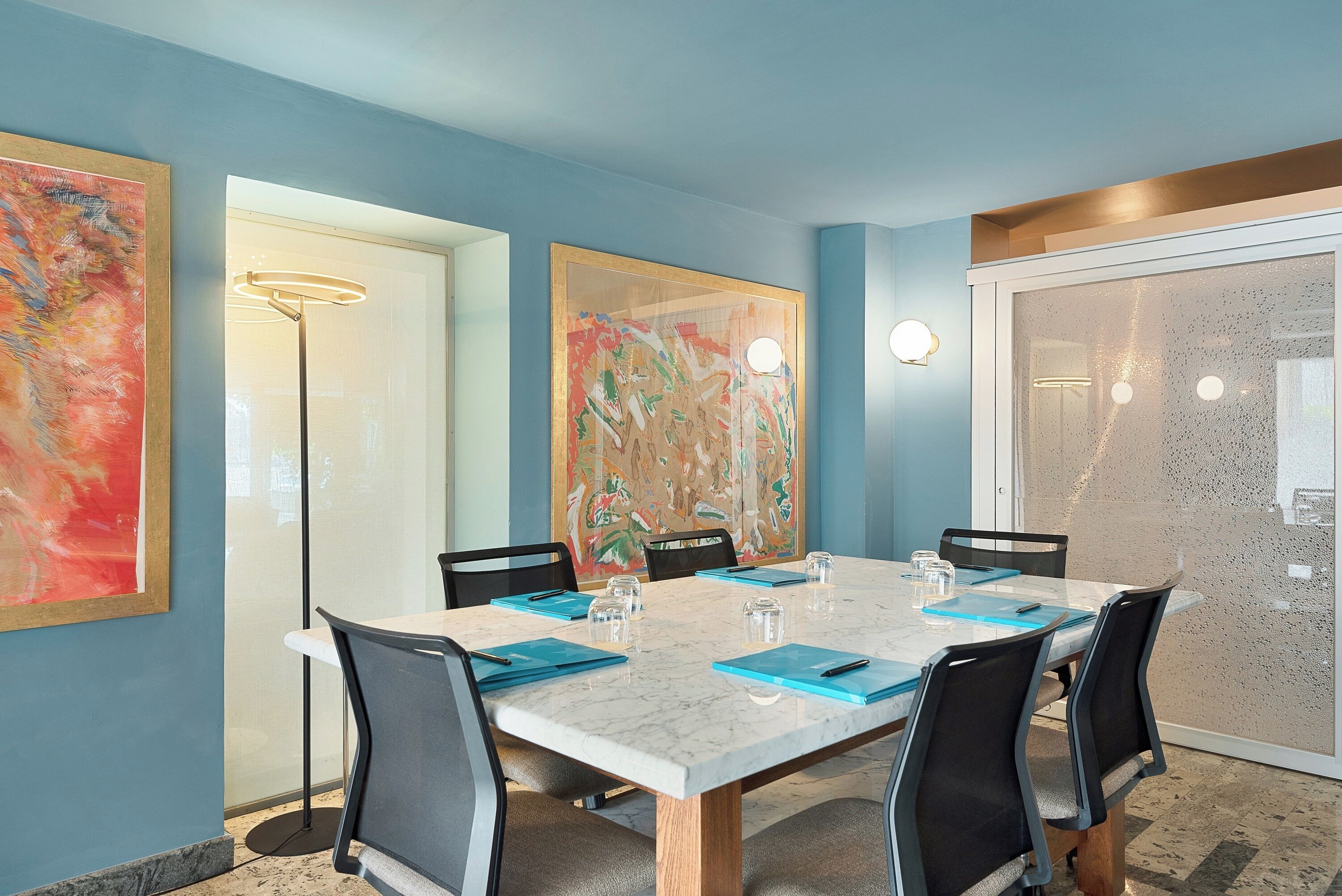 A conference room with a marble table, black chairs, and blue folders.