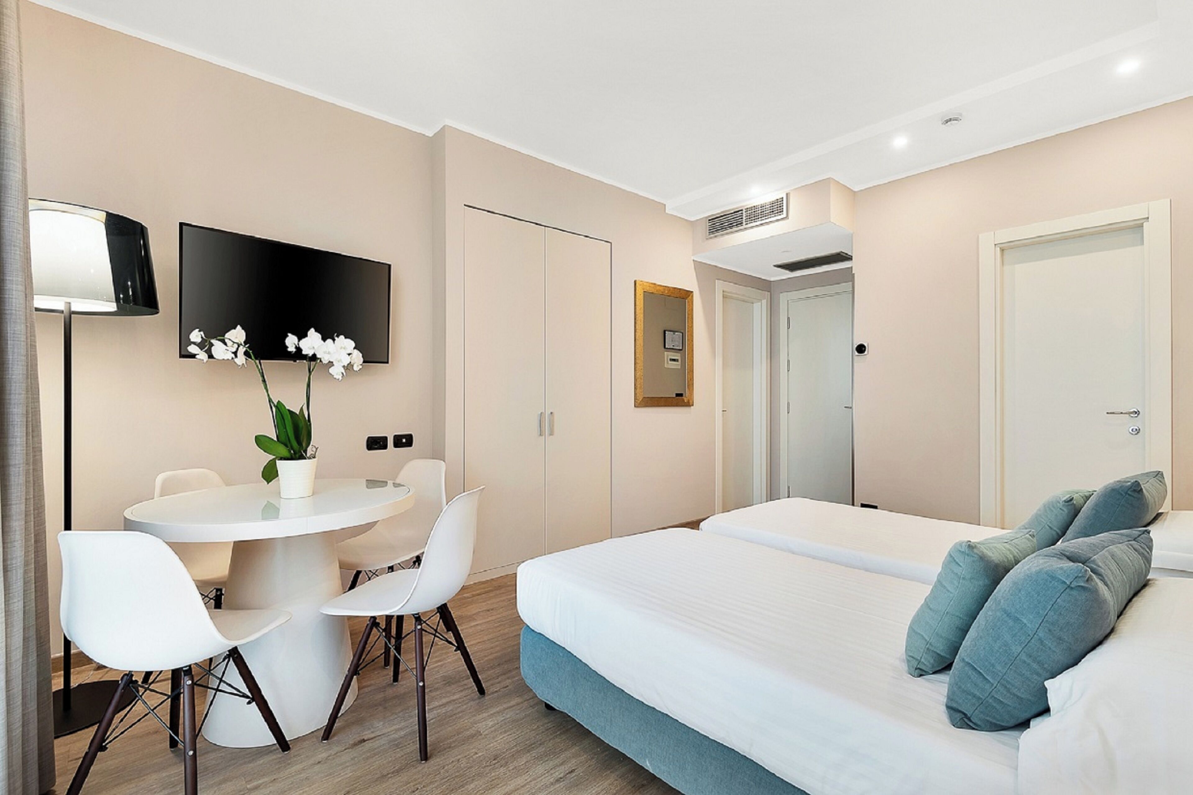 Een hotelkamer met een bed, een bureau met stoelen, een televisie en een potplant.