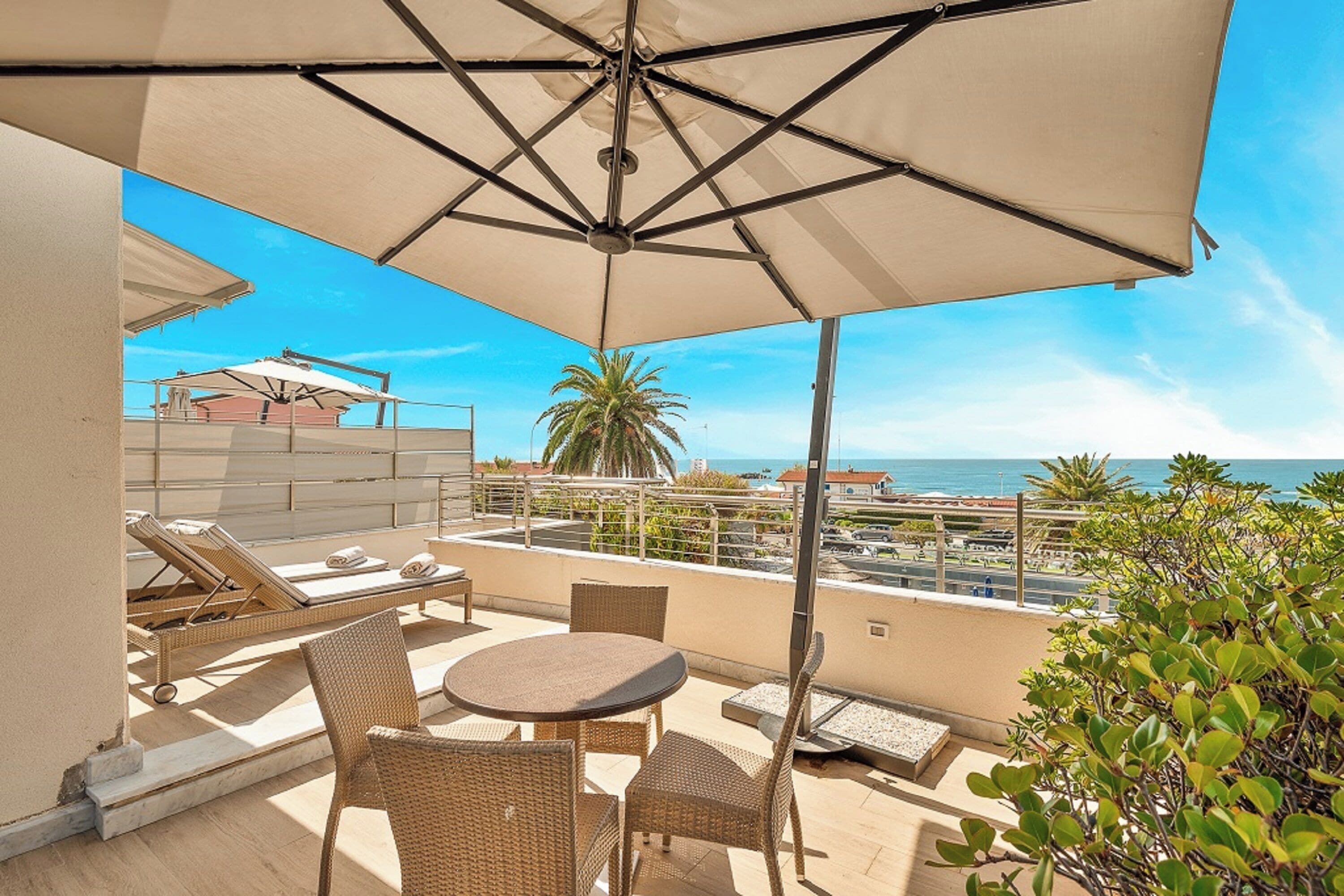 A balcony with a table and chairs, a large umbrella, and a view of the sea.