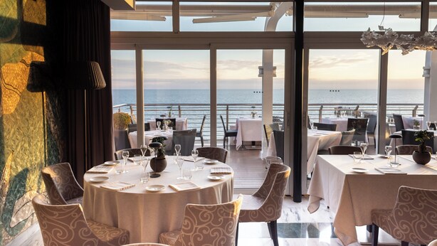 Un comedor con mesas redondas, sillas y vista al mar.