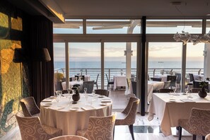 Un comedor con mesas redondas, sillas y vista al mar.