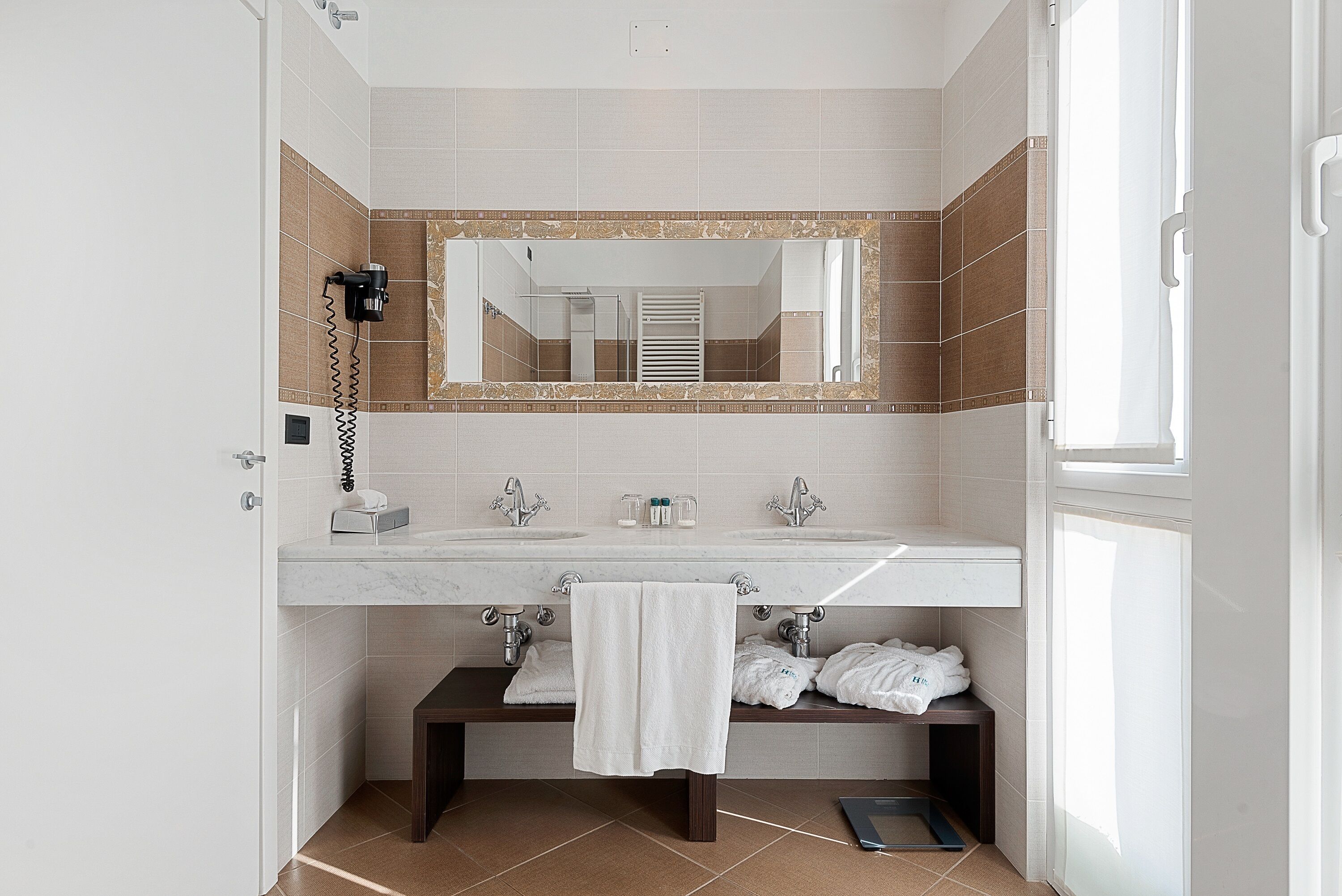 A modern bathroom with a large mirror, two sinks, a towel rack, and a shower area.