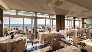 Un comedor con mesas dispuestas para los invitados, ventanas amplias que ofrecen vistas al mar y un candelabro colgando del techo.