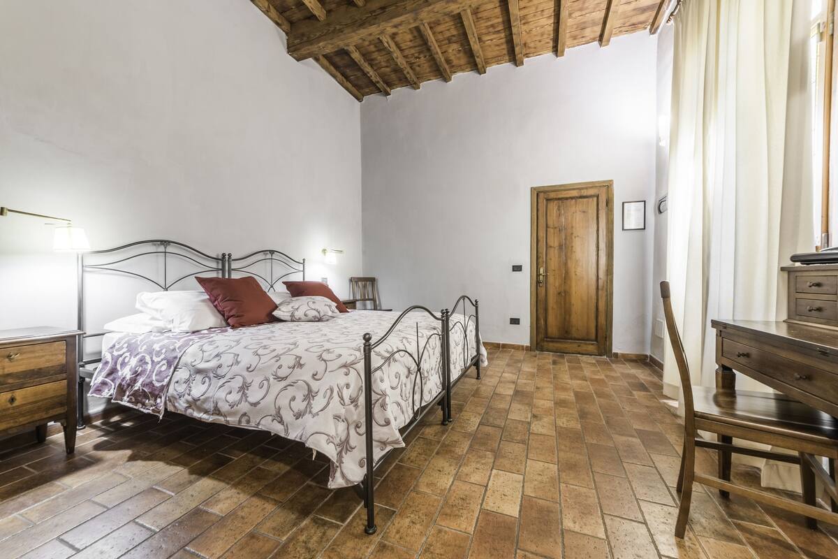 A bedroom with a bed, wooden headboard, a wooden door, a desk, and a chair.