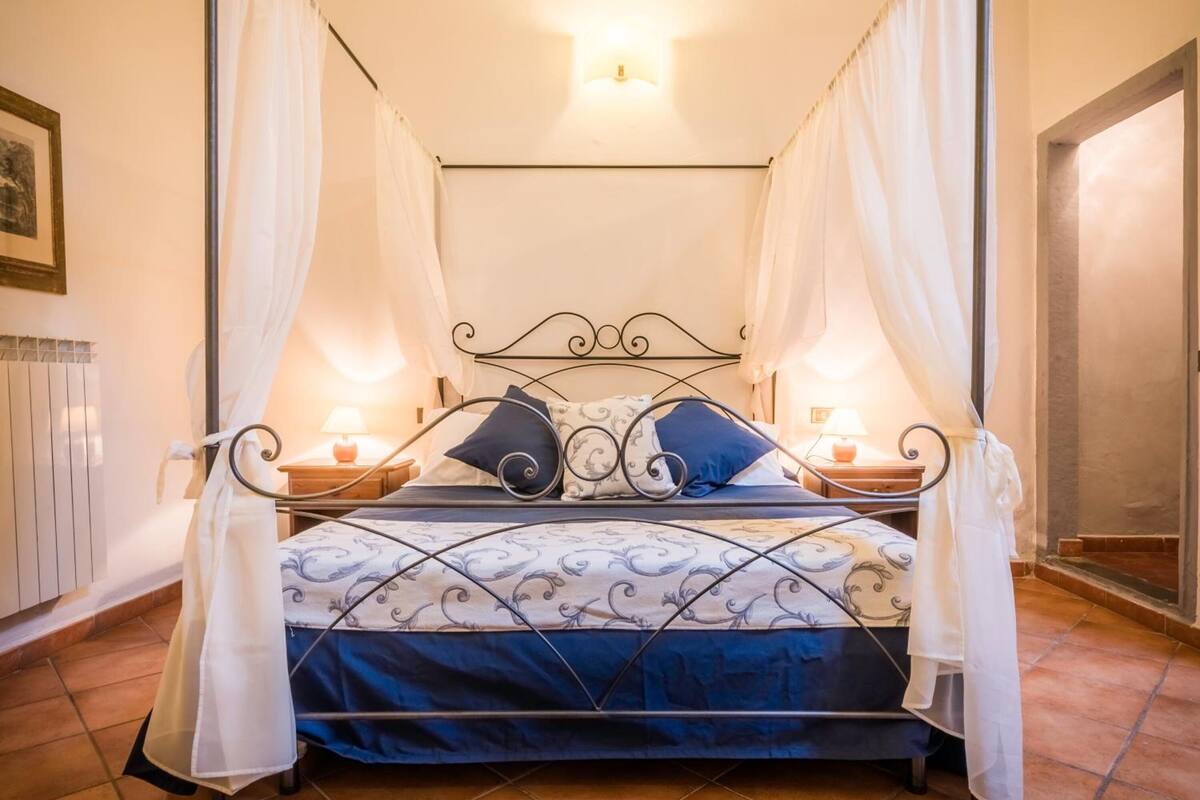 A four-poster bed with white curtains, a patterned bedspread, and two bedside lamps.