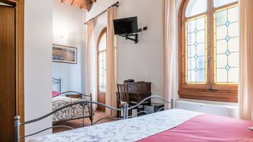 A bedroom with a wooden ceiling, a bed with a red bedspread, a desk with a chair, and a TV mounted on the wall.