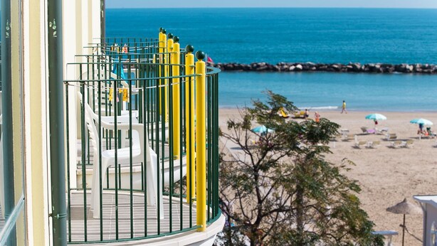 Un balcón con vista a la playa, un área de piscina y un árbol.