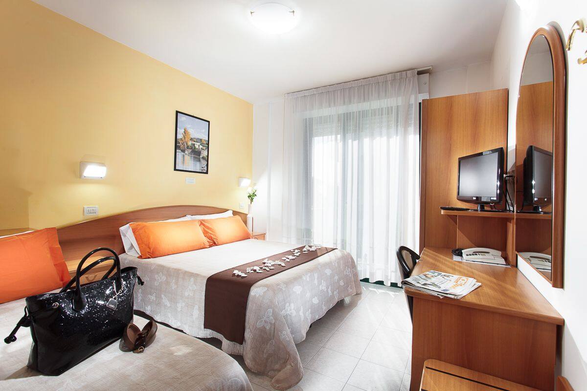 A hotel room with two beds, a desk with a computer, a mirror, and a handbag on the floor.