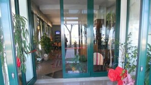 Una habitación amplia con un gran ventanal corredero que da a un balcón. El piso es de baldosas y tiene una alfombra estampada.
