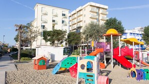 Un parque infantil en la playa con estructuras de juego de colores y un edificio al fondo.