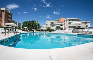 A swimming pool with sun loungers and umbrellas, surrounded by buildings with balconies and a clear sky. - Park Hotel Serena (Rimini)