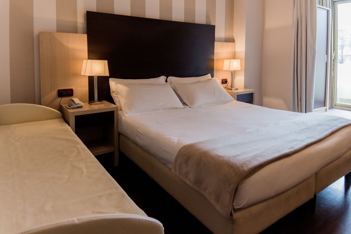 A hotel room with a large bed, two bedside tables, a nightstand, a chair, and a window with curtains.