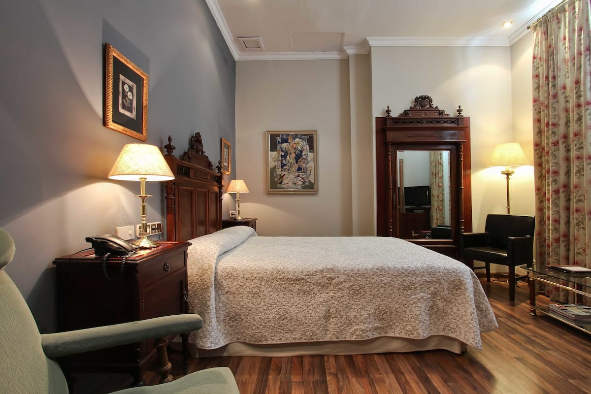 Une chambre d’hôtel comprenant un lit, deux tables de chevet, une chaise, un bureau, un miroir et une lampe.
