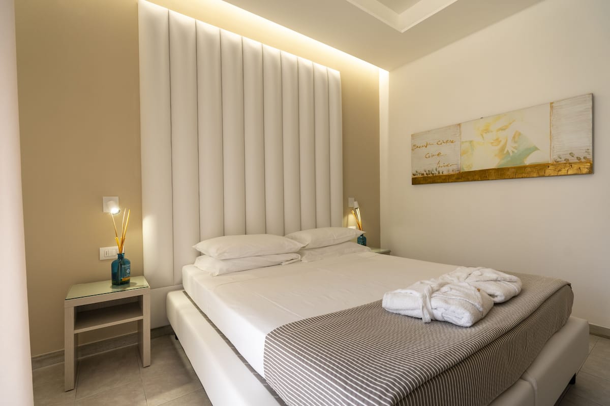 A modern bedroom with a large bed, bedside tables, and a wall-mounted artwork.