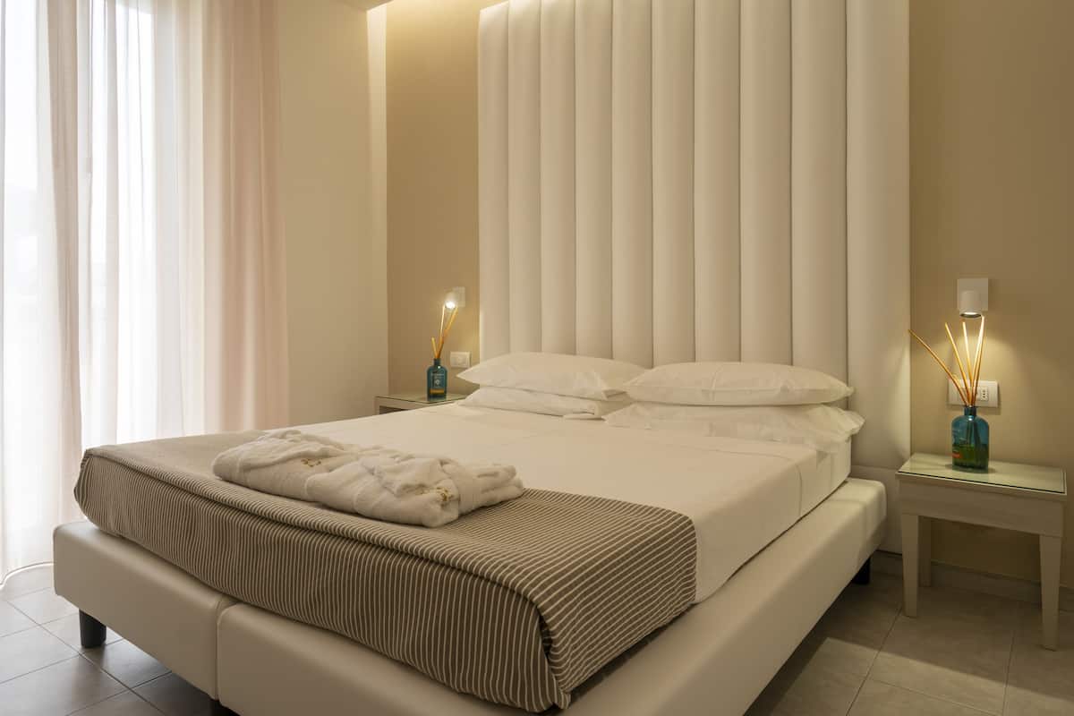 A modern hotel room with a large bed, a bedside table with a lamp, and a window with curtains.