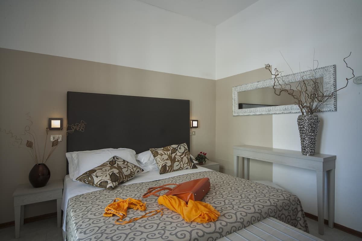 A bedroom with a bed, a nightstand, a mirror, and a vase with branches.