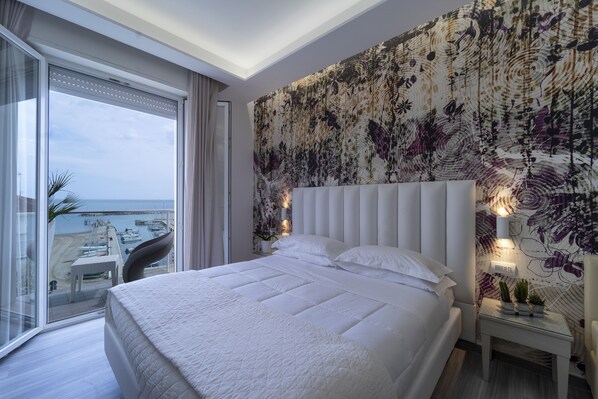 A modern hotel room with a large bed, a view of the marina, and a balcony with a table and chairs. - Hotel Stella d'Oro (Rimini)