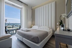 A modern hotel room with a large bed, a small desk, a view of the marina, and a balcony with a table and chairs. - Hotel Stella d'Oro (Rimini)