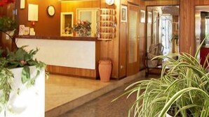 A reception area with a wooden reception desk, a clock, and a potted plant. - Hotel Haway (Cattolica)