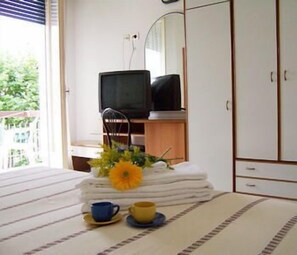 A bedroom with a bed, a television on a wooden stand, a mirror, and a window with a view of greenery outside. - Hotel Haway (Cattolica)