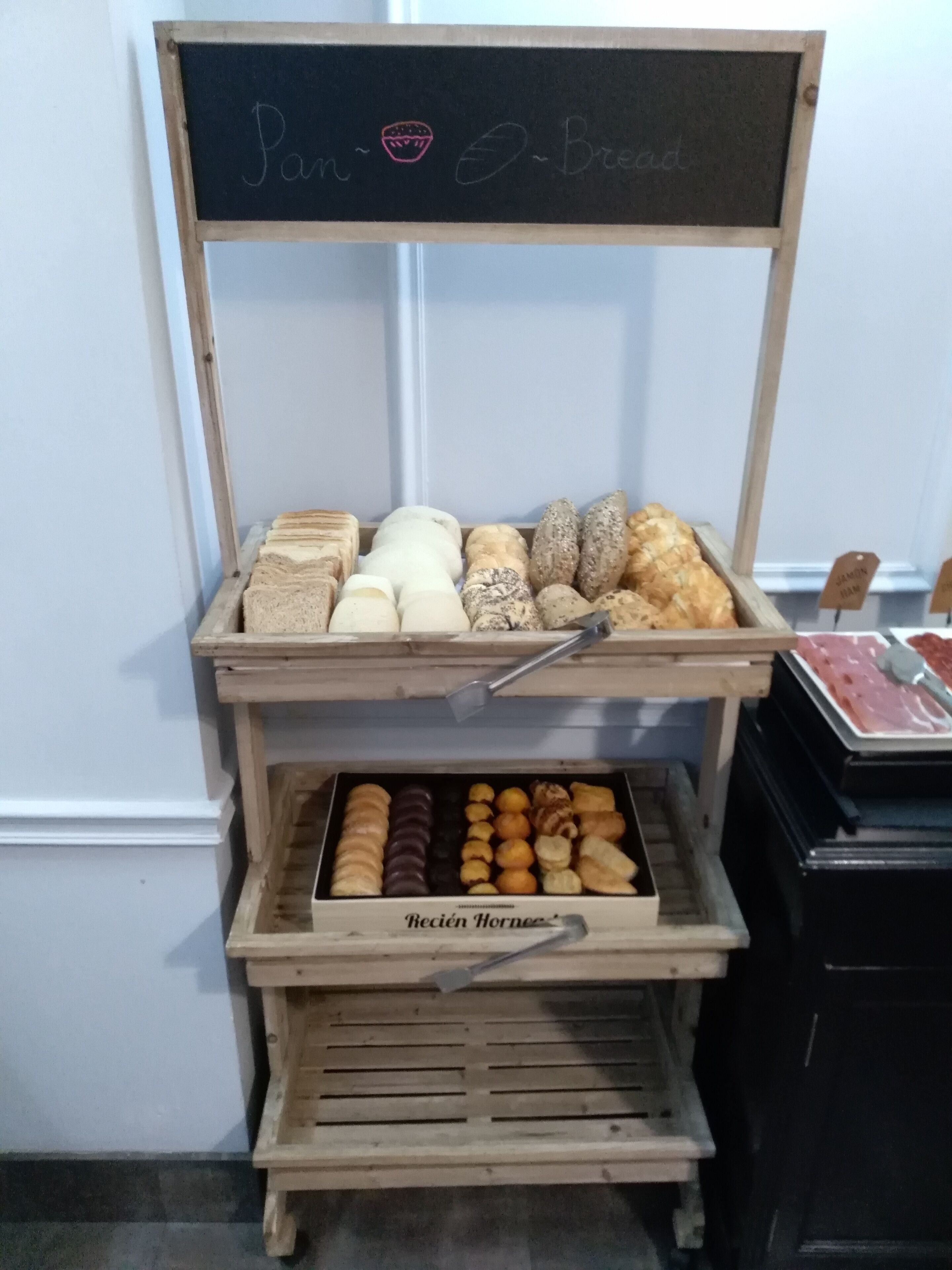 A wooden display case with various baked goods labeled "Pan Bread."