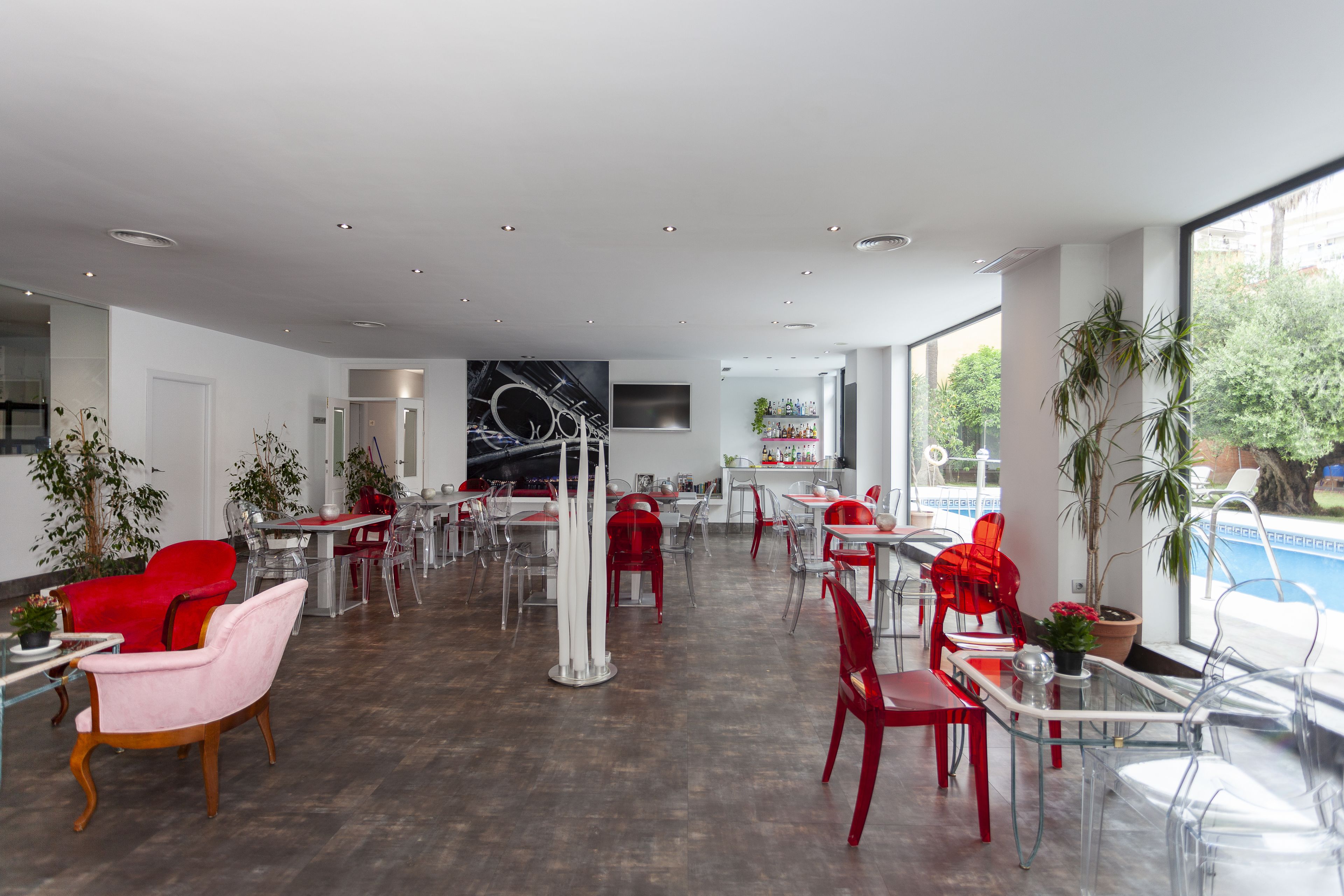 Un amplio espacio interior con varias mesas y sillas, una zona de bar y grandes ventanales con vistas al exterior.