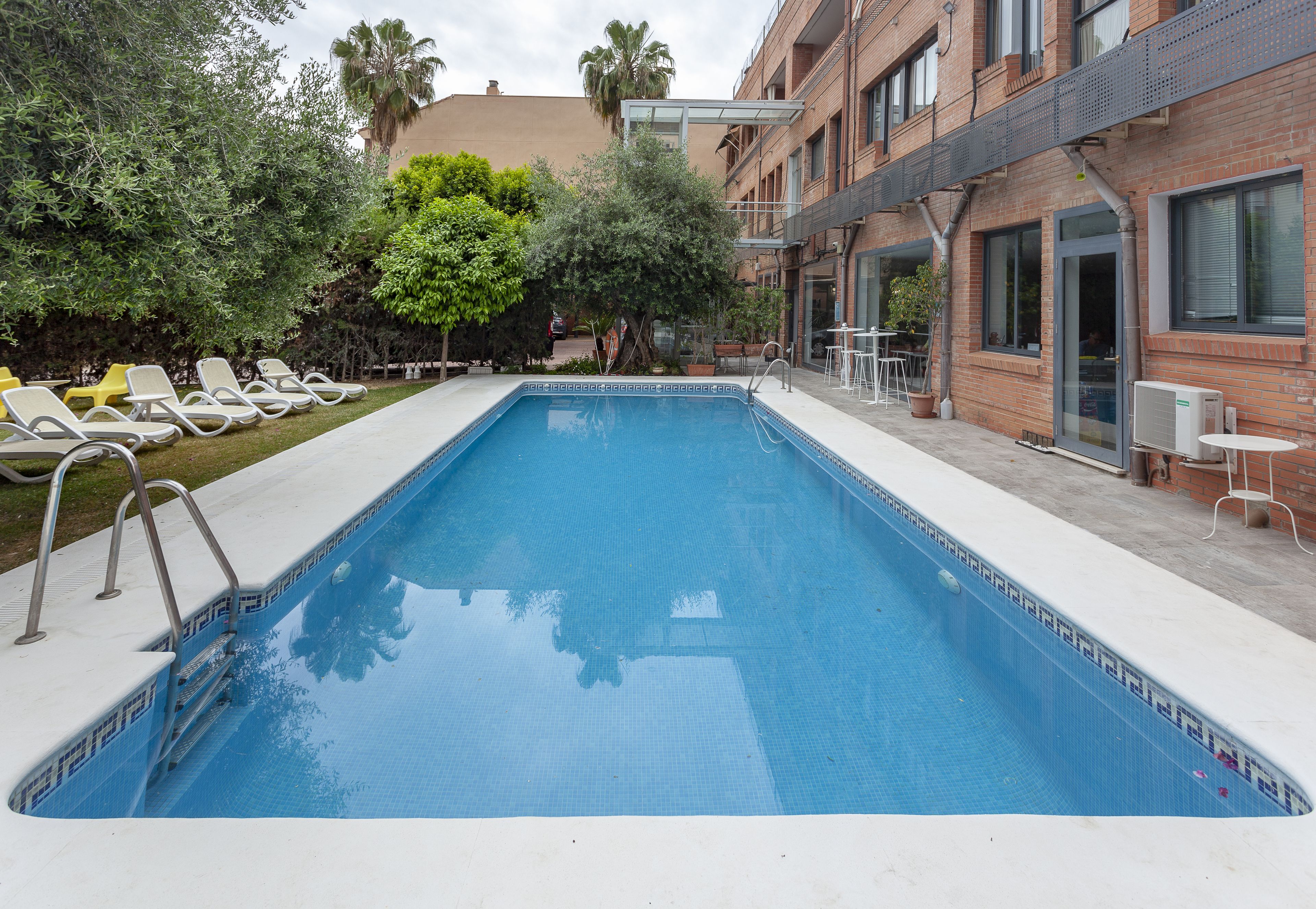 A rectangular swimming pool with a tiled edge, surrounded by a white deck. There are lounge chairs and a small table on the deck.