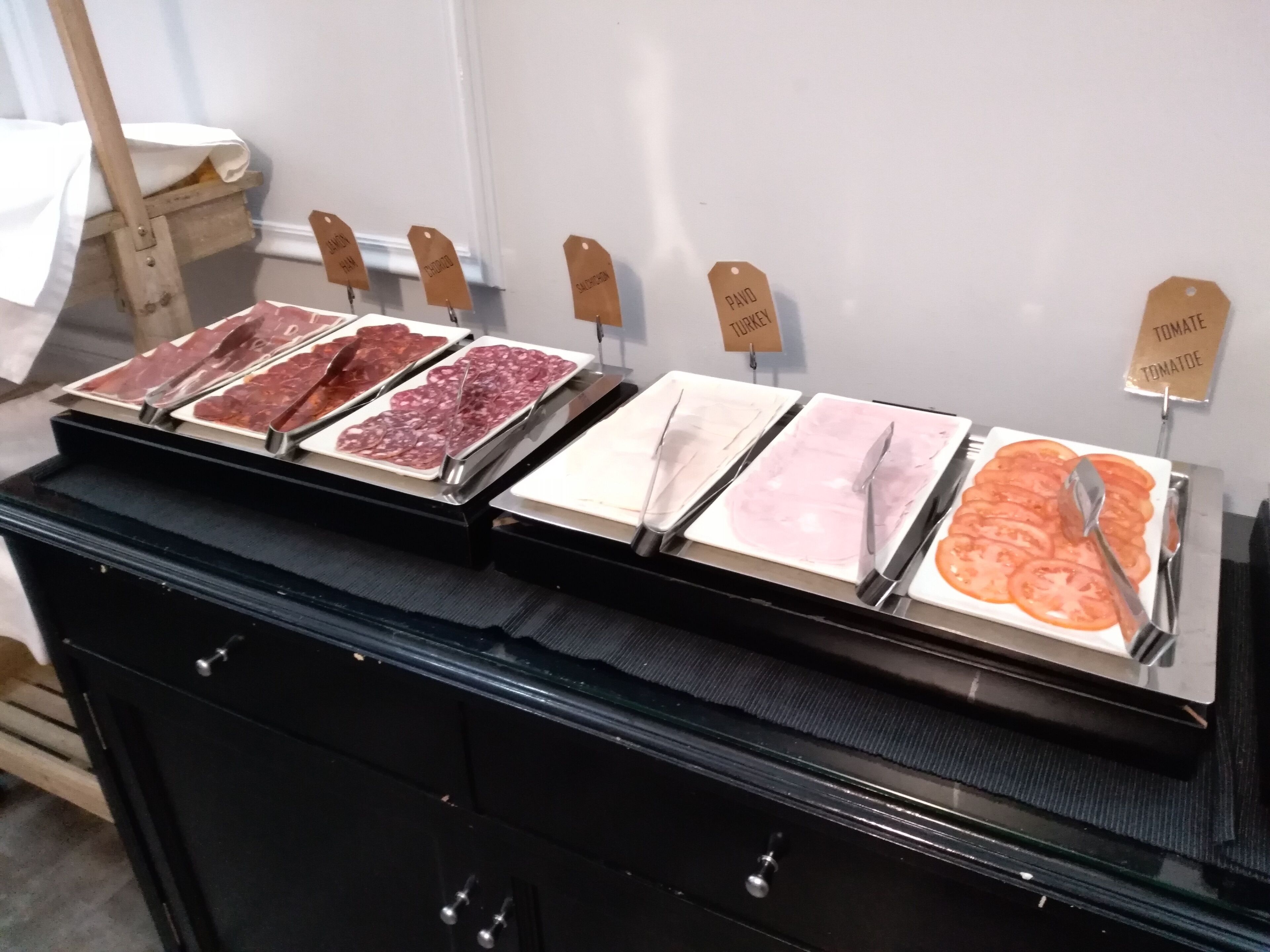 Un bufé con diversas fuentes de carne y tomate, cada una identificada con una etiqueta de madera.