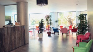 A modern lobby with a reception desk, potted plants, and colorful chairs. - Hotel AACR Monteolivos (Seville)