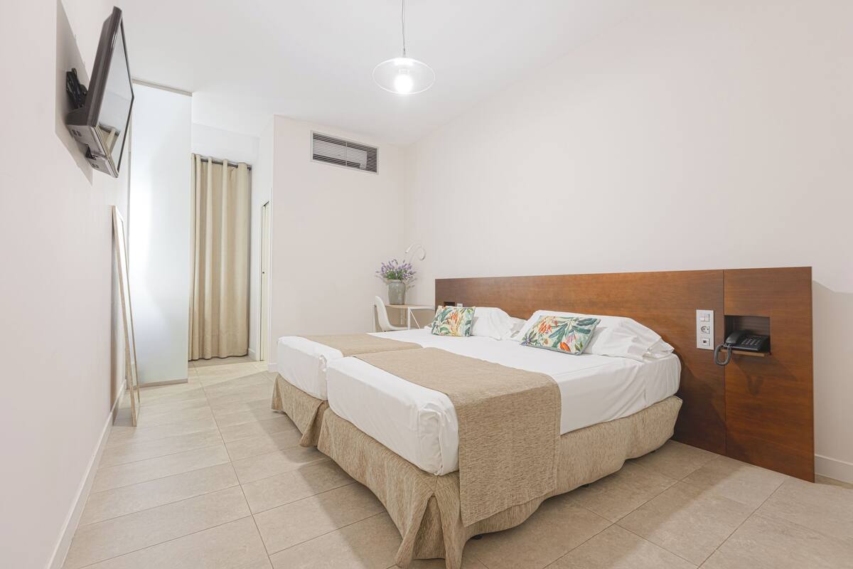 A double bed with a wooden headboard, a bedside table with a vase, and a wall-mounted phone.
